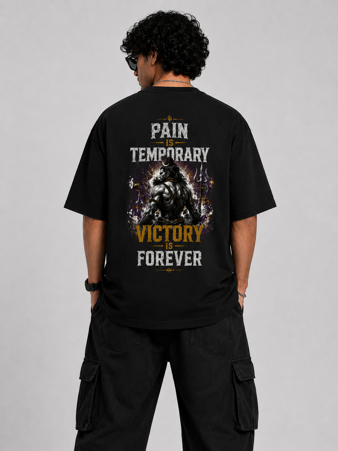 A man viewed from behind wearing a black graphic t-shirt with the text 'PAIN TEMPORARY VICTORY FOREVER' and a muscular gorilla design, paired with black cargo pants against a gray studio background.