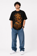 Black oversized graphic T-shirt from the StitchVaults™ GANESHA LEGACY™ Collection featuring Lord Ganesha in his Vighnaharta form standing on a lotus with an elephant illustration, saffron devotional artwork, and the sacred Ganpati Bappa Morya chant.